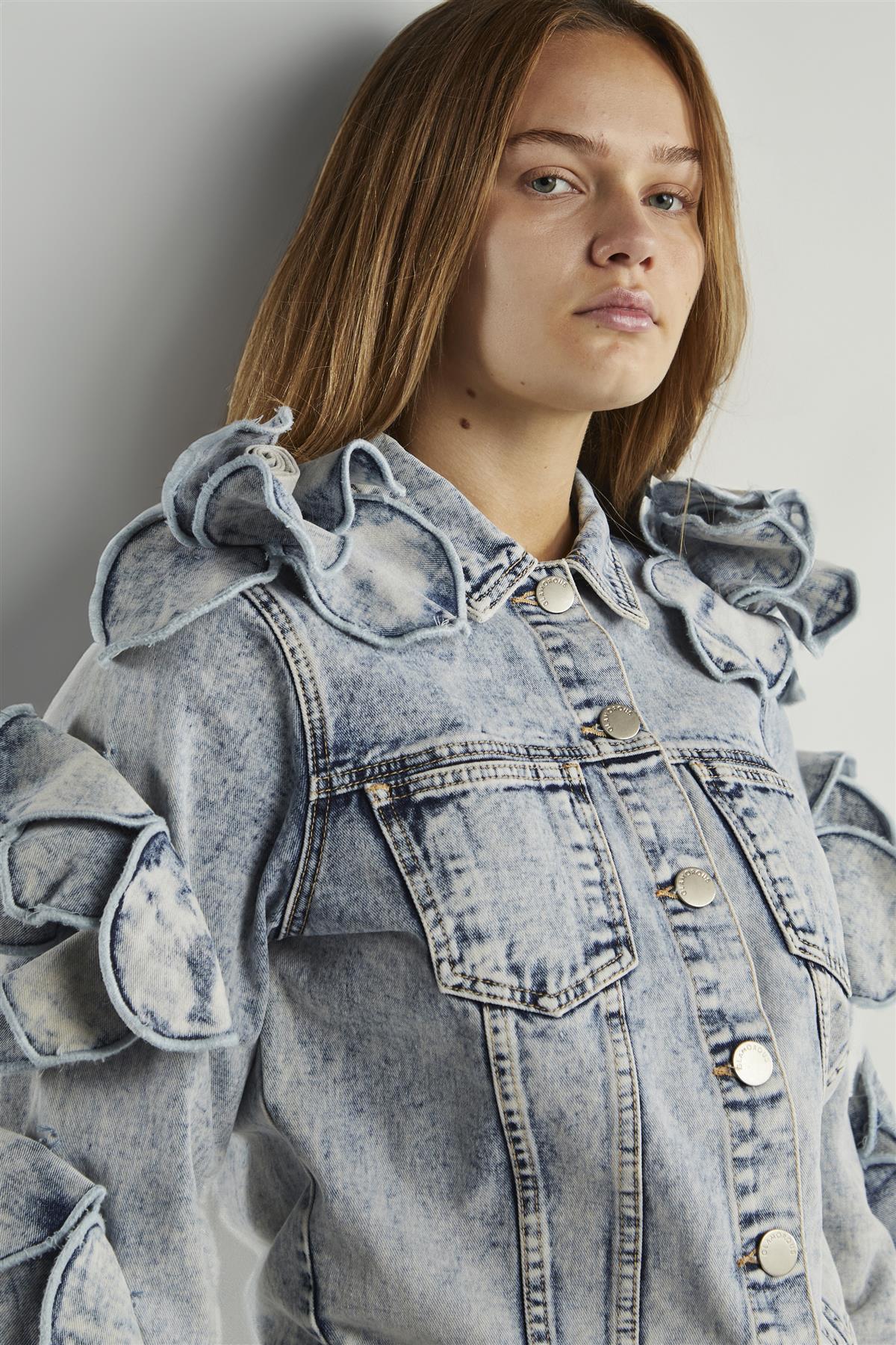 Woman wearing a denim jacket with ruffled details against a plain background
