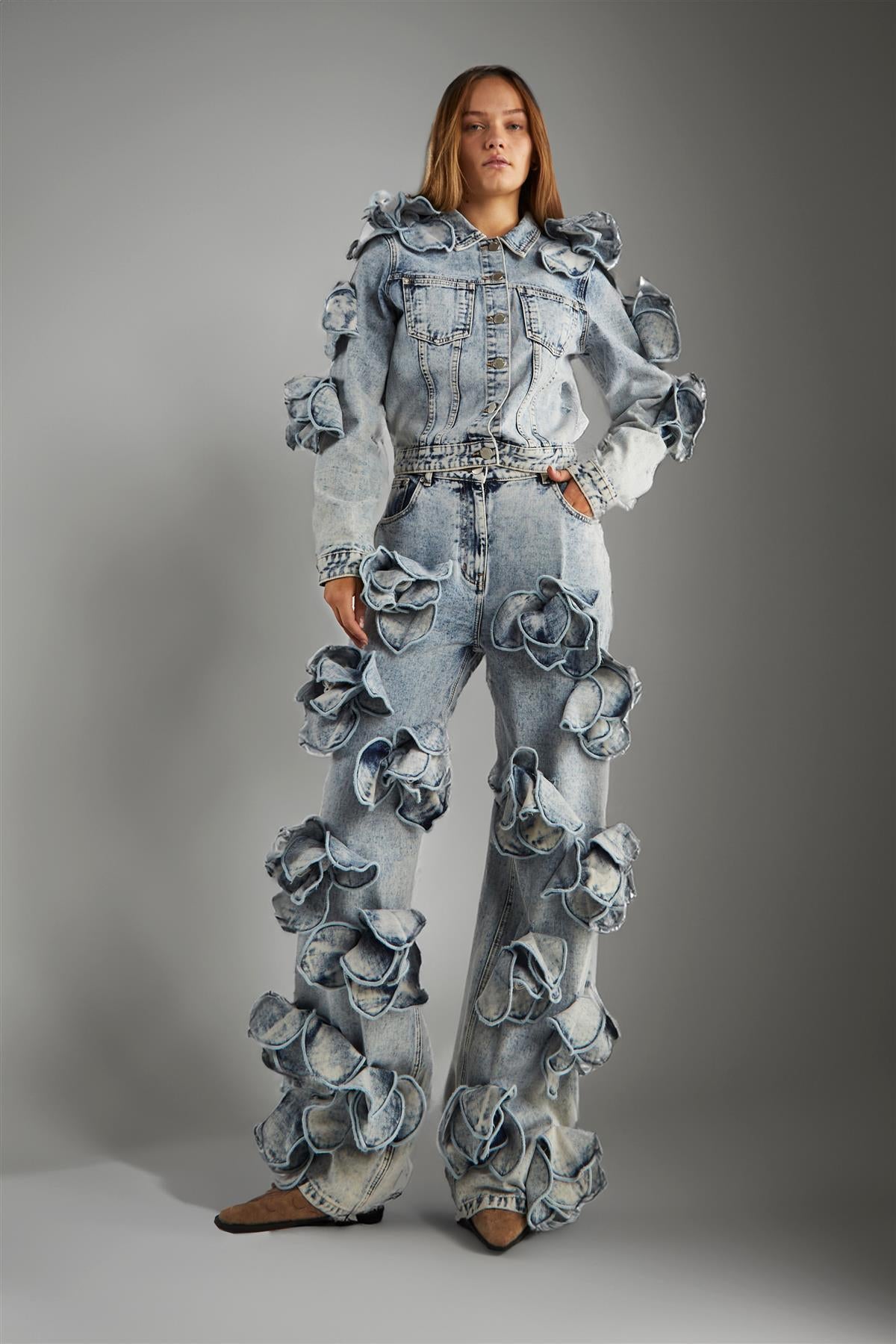 Person wearing a unique denim outfit with floral embellishments on a gray background